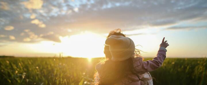 A parent and child looking towards a sunset
