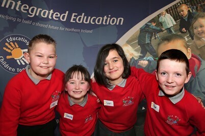Four school children stand in front of a sign saying Integrated Education