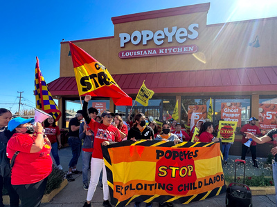 A crowd of people outside a Popeyes location holds a banner that reads: "Popeyes: Stop exploiting child labor".